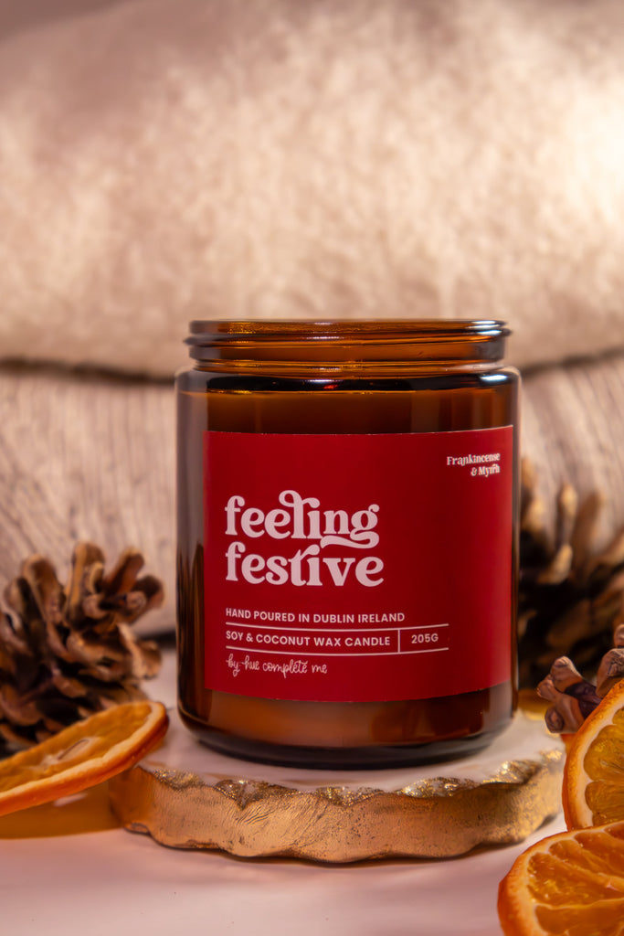 Candle labeled 'feeling festive' with decorative elements on a soft background