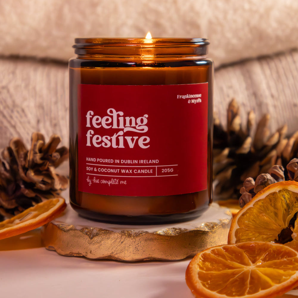 Candle in a jar labeled 'feeling festive' with decorative elements on a neutral background