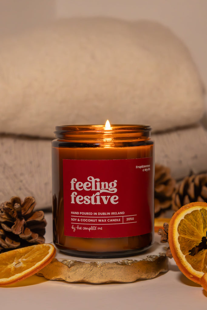 Candle labeled 'feeling festive' with decorative elements on a neutral background