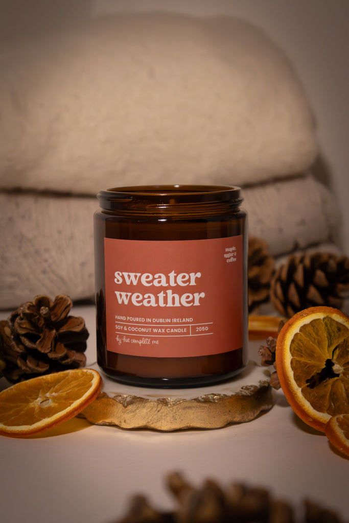 Candle labeled 'sweater weather' with decorative elements on a soft background