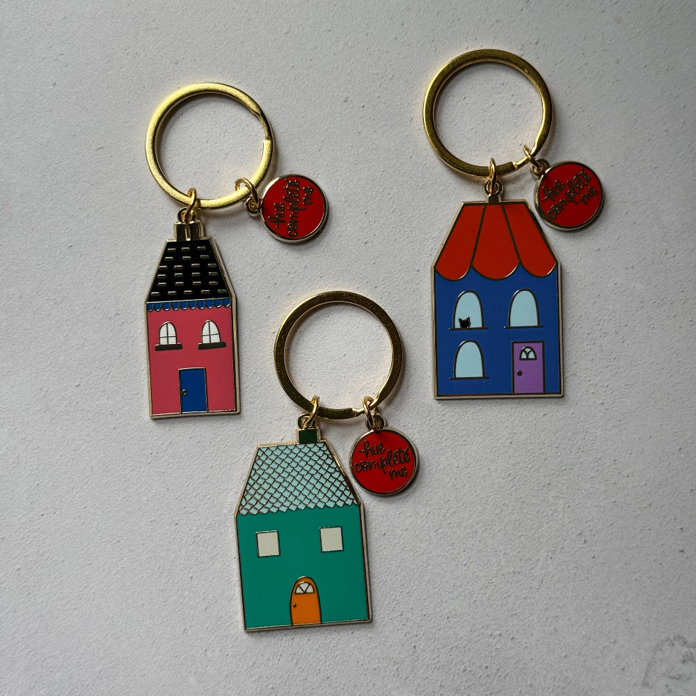 Three colorful house-shaped keychains on a gray background