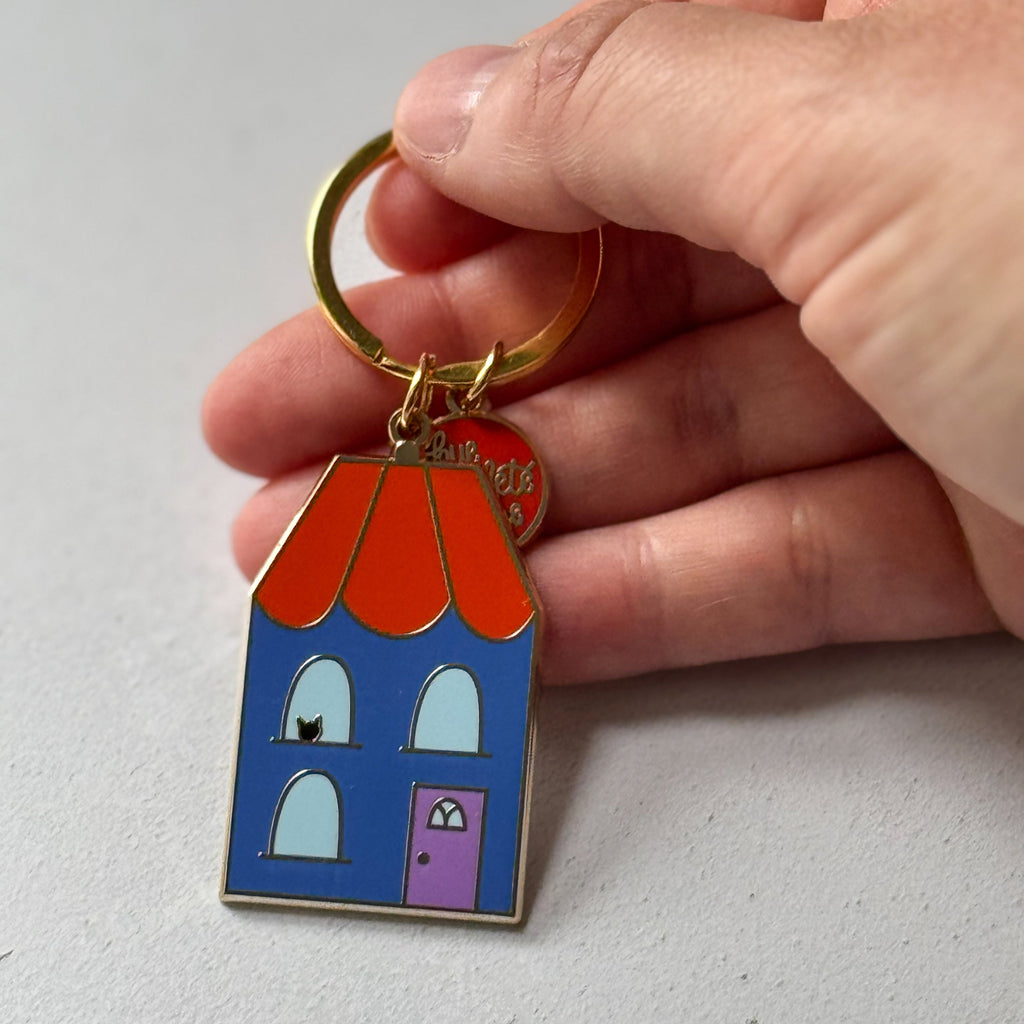 House-shaped keychain with a red roof held by a hand on a light gray background