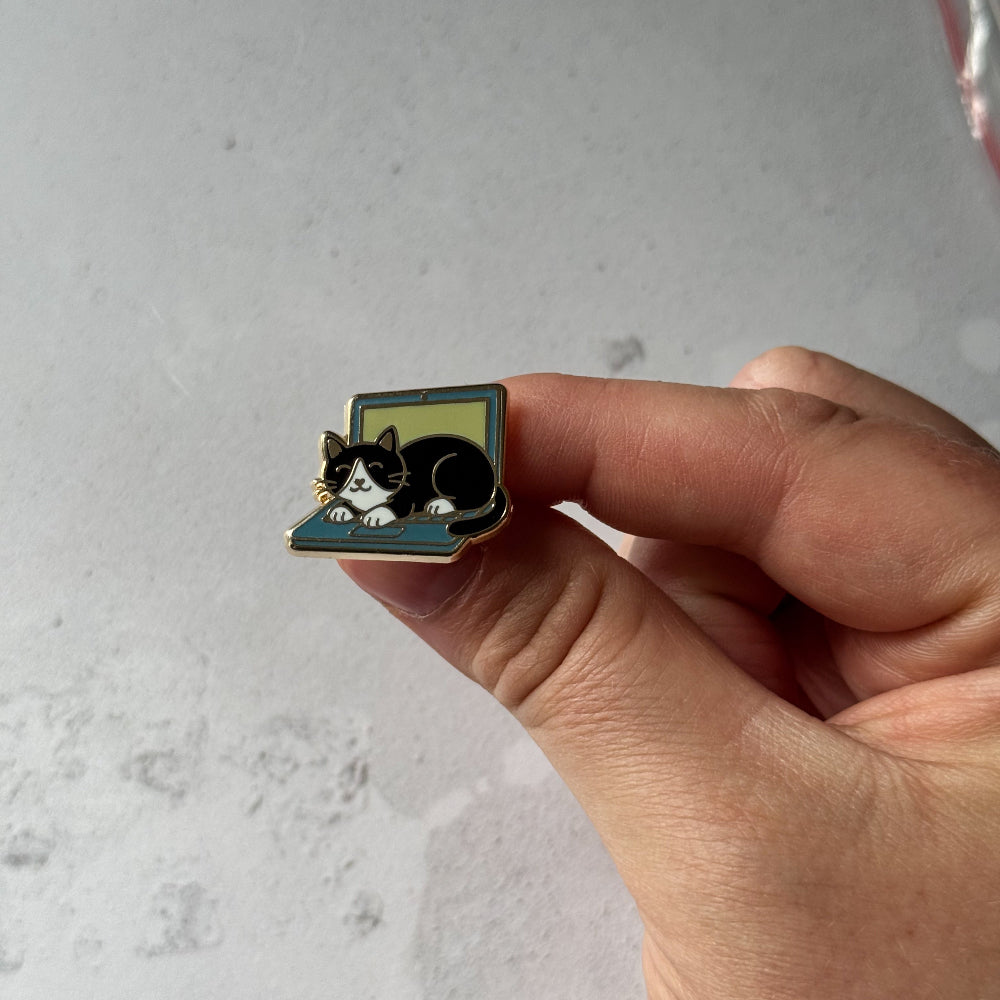 Hand holding a small pin with a cat design against a light gray background