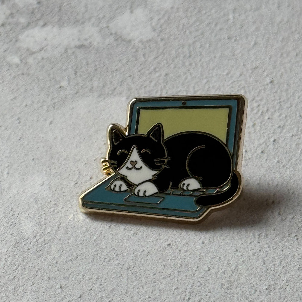 Enamel pin of a black and white cat on a laptop on a light gray background