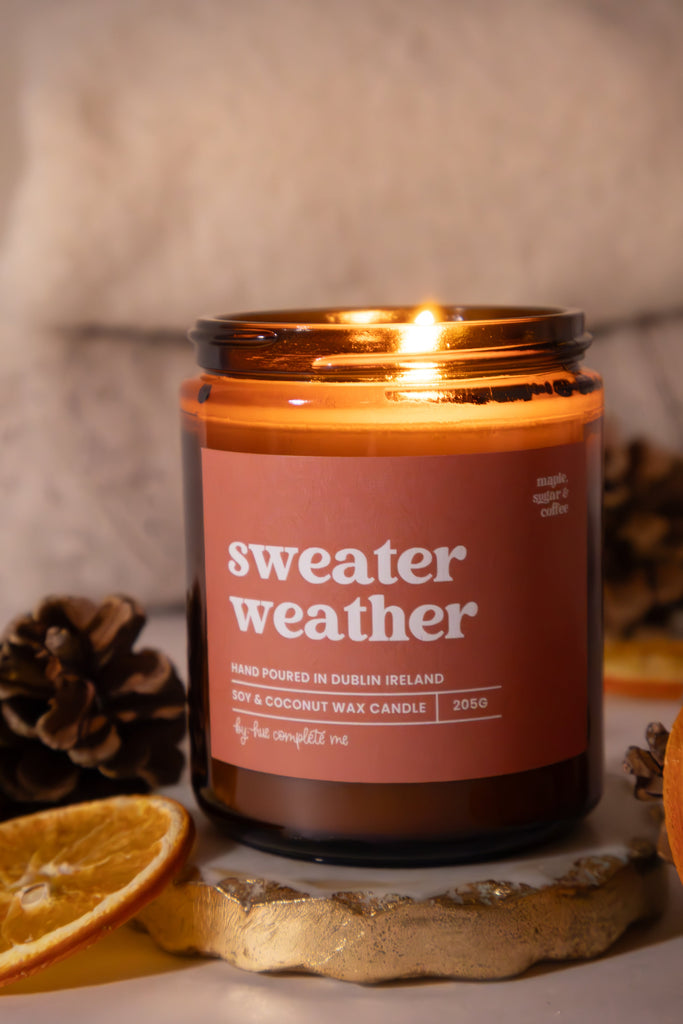 Candle labeled 'sweater weather' with decorative elements on a neutral background