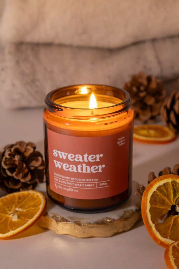 Candle labeled 'sweater weather' with decorative elements on a neutral background