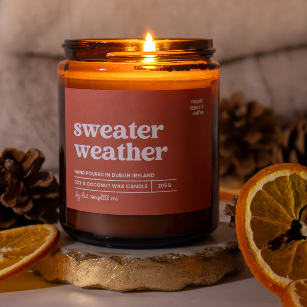 Candle labeled 'sweater weather' with decorative elements on a surface